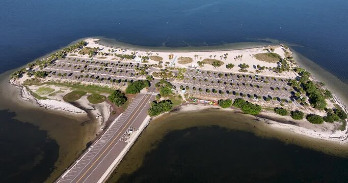 Aerial view of Fred Howard Park in Tarpon Springs, Florida, featuring parking lots, palm trees, sandy beaches, and surrounding blue waters under a clear sky.
