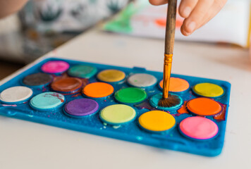 Child draws with watercolor paints hnad closeup. Chilren creativity,art an craft concept.