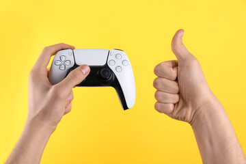Man using wireless game controller and showing thumbs up on yellow background, closeup © New Africa