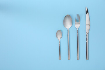 Stylish silver cutlery set on light blue background, flat lay. Space for text