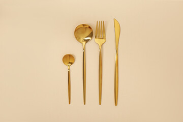 Stylish golden cutlery set on beige background, flat lay