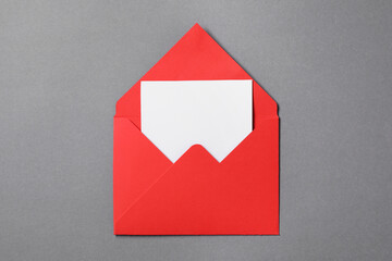 Blank sheet of paper in open letter envelope on grey background, top view