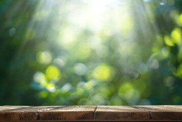 The rustic wooden aged textured table surface in the summer garden in front of the unfocused green sunshine background. Display for natural organic products.