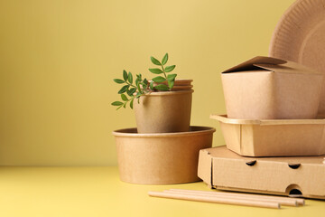 Eco friendly food packaging. Paper containers, tableware and green twigs on pale yellow background, space for text
