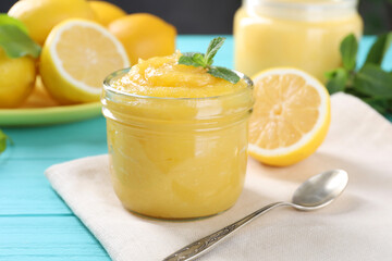 Delicious lemon curd in glass jar, fresh citrus fruits, mint and spoon on light blue wooden table