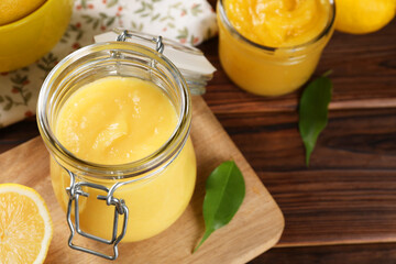 Delicious lemon curd in glass jars, fresh citrus fruit and green leaves on wooden table