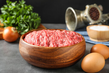 Raw ground meat in bowl and different products on grey table