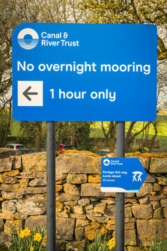 A Spring HDR portrait image of a blue Canal and River Trust sign on towpath with white lettering giving mooring and portage information.