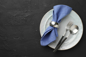 Stylish setting with cutlery, napkin and plate on dark textured table, top view. Space for text