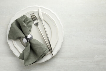 Stylish setting with cutlery, napkin and plates on light textured table, top view. Space for text