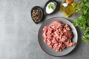 Raw ground meat, spices, parsley and oil on grey table, flat lay. Space for text