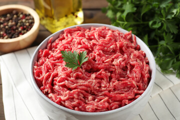 Raw ground meat in bowl, parsley, spices and oil on table, closeup