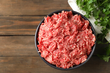 Raw ground meat in bowl and parsley on wooden table, top view. Space for text