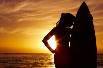 Silhouette, sunset and woman surfer at ocean for outdoor training, vacation and holiday. Summer, waves and shadow of beach coast for health, surfing and lens flare with dark surfboard in nature