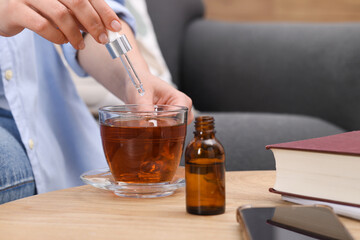 Woman dripping food supplement into cup of tea at wooden table indoors, closeup