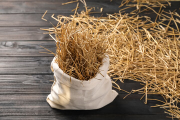 Dried straw in burlap sack on dark wooden table, space for text