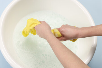 Woman washing baby clothes in basin on light blue background, closeup