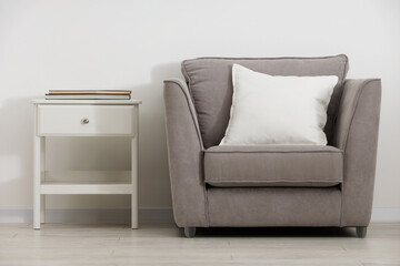 Soft white pillow on armchair and bedside table near light wall indoors
