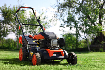 Obraz premium Modern lawn mower on green grass in garden