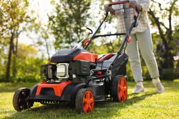 Woman cutting green grass with lawn mower in garden, selective focus