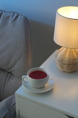 Cup of hot tea and nightlight on white table at night
