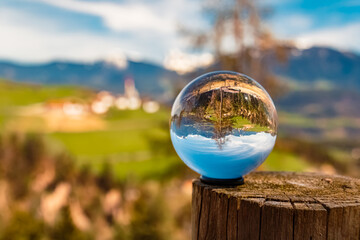 Crystal ball alpine spring landscape shot with a church in the background seen from near Klobenstein, Ritten, Eisacktal valley, South Tyrol, Italy