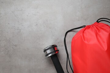 Red drawstring bag and dumbbell on grey textured background, flat lay. Space for text