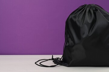 Black drawstring bag on white wooden table against purple background. Space for text
