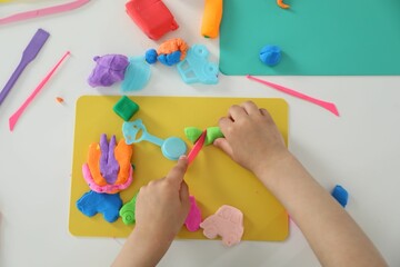 Little girl sculpting with play dough at white table, top view