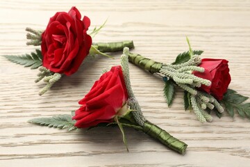 Many stylish red boutonnieres on light wooden table