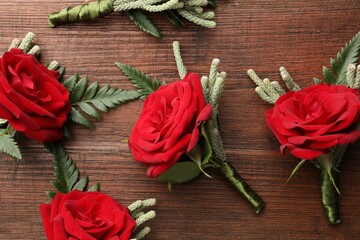 Many stylish red boutonnieres on wooden table, flat lay