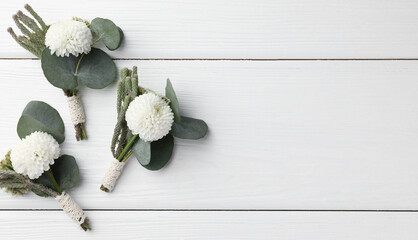 Small stylish boutonnieres on white wooden table, flat lay. Space for text