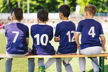 Multiethnic Kids in Soccer Jersey Shirts Sitting on Substitute Wooden Bench. School Children at...