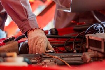 Close-up of Asian male mechanic in grey uniform adjusting car engine in auto repair shop. Scene emphasizes hands-on approach, attention to detail, and professional automotive maintenance service.