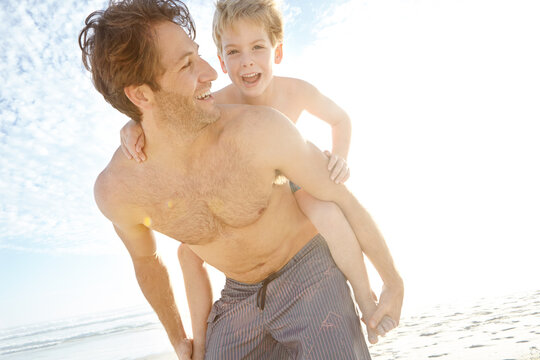 Dad, boy and happy in beach with piggyback on holiday in summer, bonding and support in Miami. Parent, kid and smile or excited with fun at seaside on vacation, trip and travel for child development