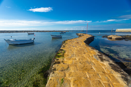 A yellow stone pier jutting out into the blue sea. Point Penmarc'h, Brittany, France.