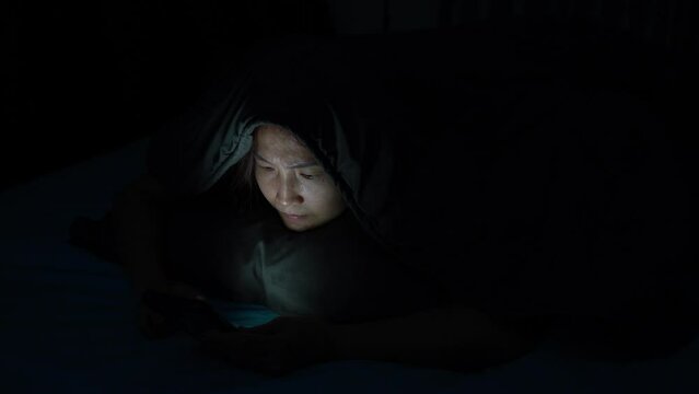 Young Woman Addicted to Social Media, Lying in the Dark Bedroom, Struggling with Insomnia and Strained Eyes from Nighttime Scrolling and Online Shopping