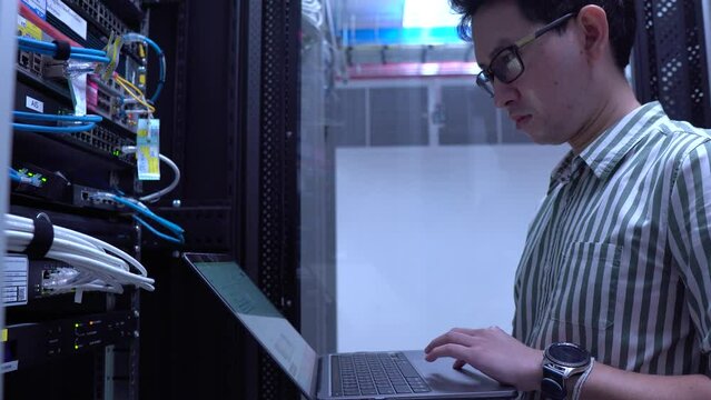 A Computer Engineer Working in a Large Data Center, Surrounded by Advanced Technology and Modern Servers, Managing and Monitoring the Factory's Cutting-Edge IT Infrastructure in a High-Tech Facility