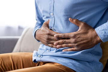 A man is shown clutching his stomach in pain, experiencing abdominal discomfort suggesting...