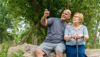 A smiling man sitting next to an elderly woman, using a phone, in the park.
