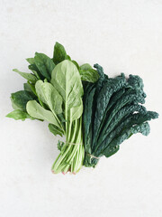 Bundles of fresh green spinach and Lacinato kale on light colored granite countertop, high angle view with copy space.