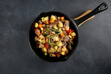 Top view of a hearty skillet beef ragout with mixed vegetables on a textured black backdrop