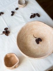 A large plate made of beige ceramics on a table covered with a linen tablecloth. Flat layout, top view. The plate is brown, natural color. Dried alder seeds are on the plate.