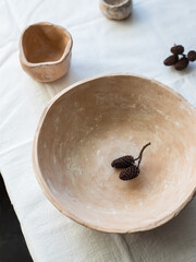 A large plate made of beige ceramics on a table covered with a linen tablecloth. Flat layout, top view. The plate is brown, natural color. Dried alder seeds are on the plate.