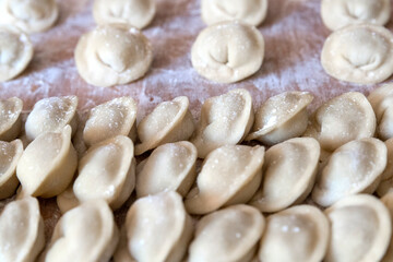 The raw dumplings were placed on a wooden cooking board, sprinkled with flour. The filling is minced meat, potatoes, cheese or cottage cheese. A semi-finished product, ready for cooking.