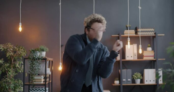 Loop of cheerful businessman dancing to music in illuminated office having fun at work at night. Emotion and creative workplace concept.