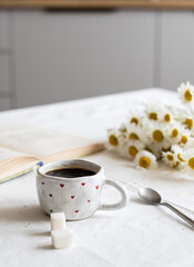 Morning coffee. There is a book on the table, a bouquet of daisies and a mug of coffee.