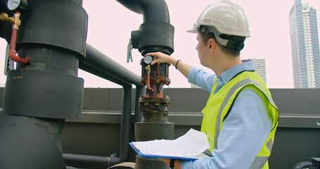 A Engineer man looking inspecting maintenance insulated pipelines valve pump control on the roof at...
