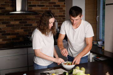 Joyful young couple enjoying cooking together in kitchen. Man and woman are preparing vegetable...