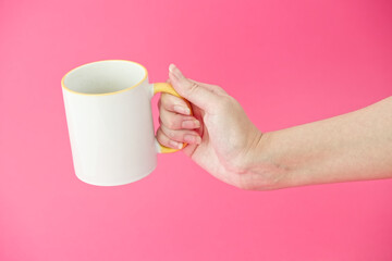 Woman's hamd holding coffee, tea ceramic cup on a pink background. White mug in the frame. Isolated studio photo. 